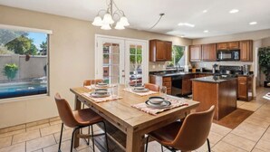 A modern kitchen with wooden cabinets, a central island, and a dining area with a wooden table and chairs. - Spacious Home in Prime Location | Pool, Spa, Games (Glendale)