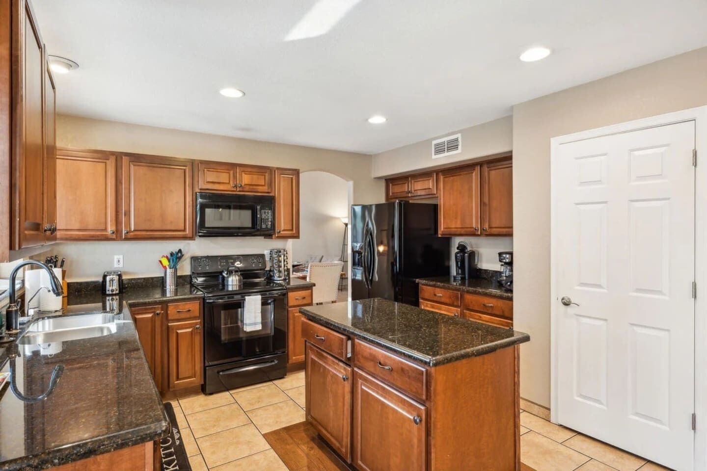 A kitchen with wooden cabinets, a black stove, a microwave, and a refrigerator.