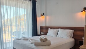 A neatly made bed with pillows and rolled towels, a bedside lamp, and a view through sheer curtains to the outdoors. - Rigani Gökçeada (+14)  (Gokceada)