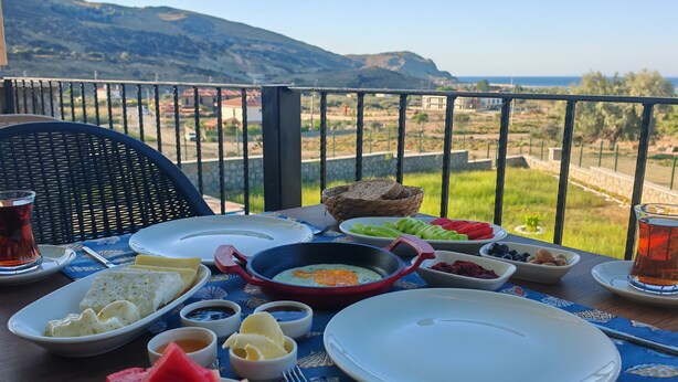 A table set with breakfast items, including eggs, bread, and fruit, on a balcony with a scenic view. - Rigani Gökçeada (+14)  (Gokceada)