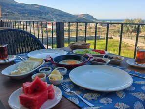 Ein Tisch ist reichhaltig mit Frühstücksangeboten gedeckt, darunter Eier, Brot und Obst, auf einem Balkon mit herrlicher Aussicht.