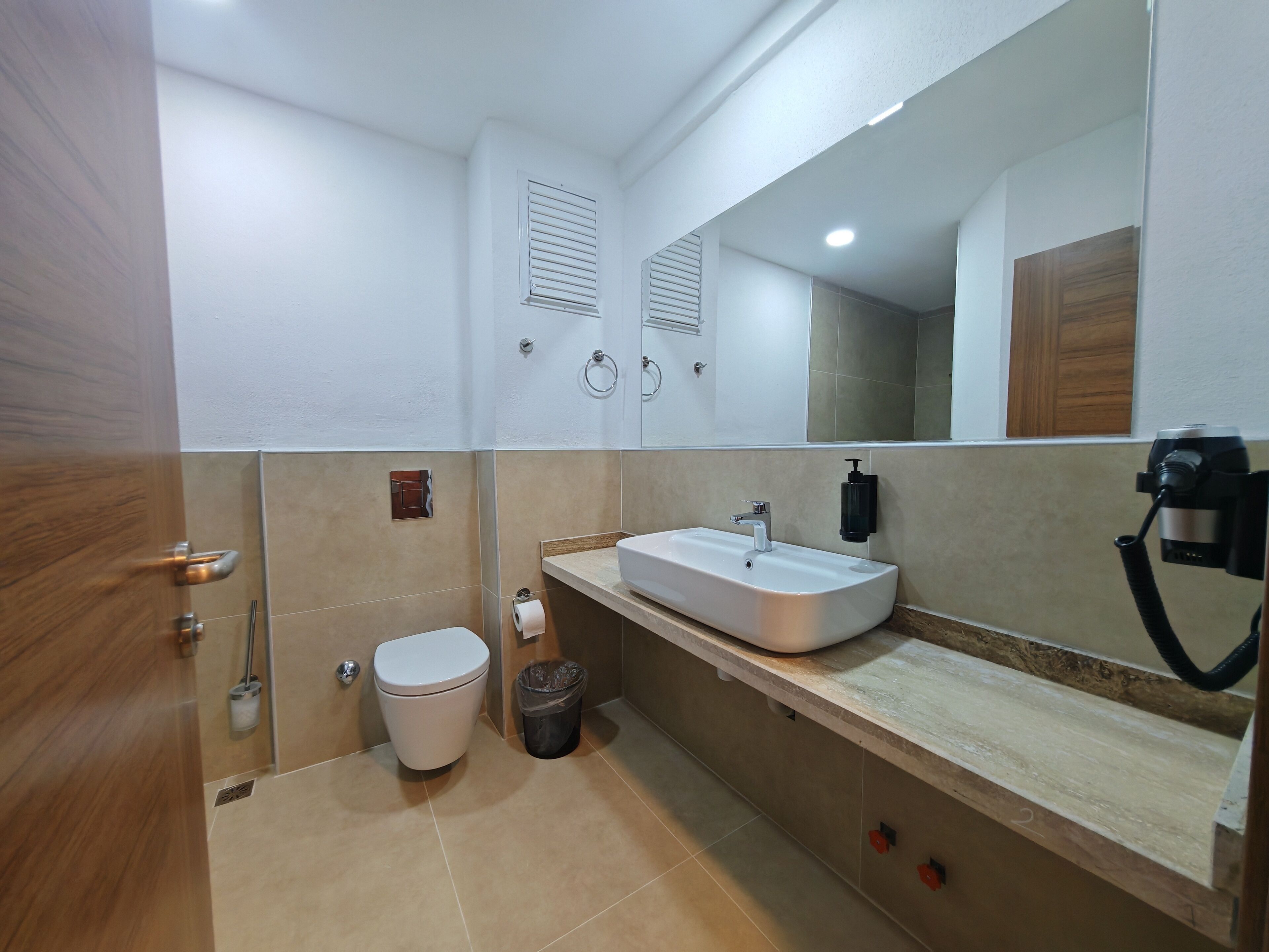 Un baño moderno con un inodoro blanco, un lavamanos con espejo y un cubo de basura.