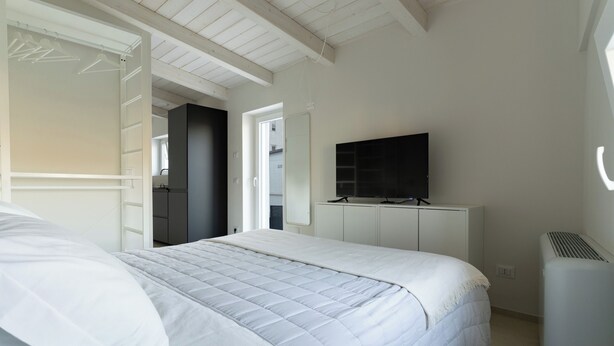 A bedroom with a bed, a TV on a stand, and a wardrobe. - Sassi di Matera loft with terrace - free parking (Matera)