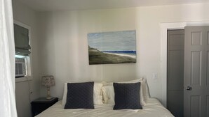 Een slaapkamer met een bed, een schilderij van een strand, een bedlampje en een gesloten deur.