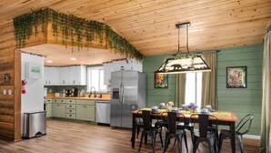 A kitchen with wooden cabinets, a stainless steel refrigerator, and a dining area with a table set for four. - Storybook Summit: Theater, Arcade, Spa, and more! (Big Bear Lake)