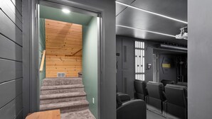 A modern interior with a staircase leading to a wooden ceiling, a seating area with black chairs, and a projector mounted on the ceiling. - Storybook Summit: Theater, Arcade, Spa, and more! (Big Bear Lake)
