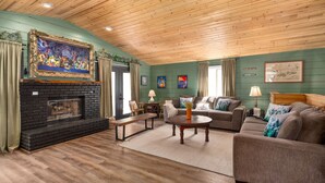 A cozy living room with a fireplace, wooden ceiling, green walls, and comfortable seating. - Storybook Summit: Theater, Arcade, Spa, and more! (Big Bear Lake)