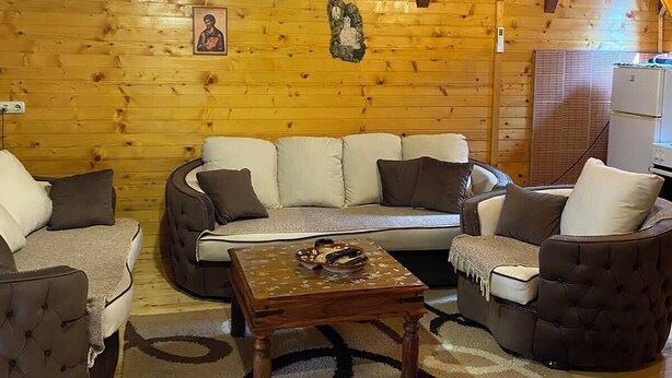 Ein Blockhaushaus-Innenraum mit Holzboden, einer Sofagarnitur, einem Couchtisch und einem Kühlschrank.