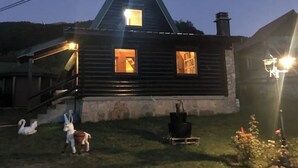 Eine Holzdiele mit Satteldach, einer Treppe zu einer Veranda und einem kleinen Garten mit Vogelhaus und Kaninchenfigur.