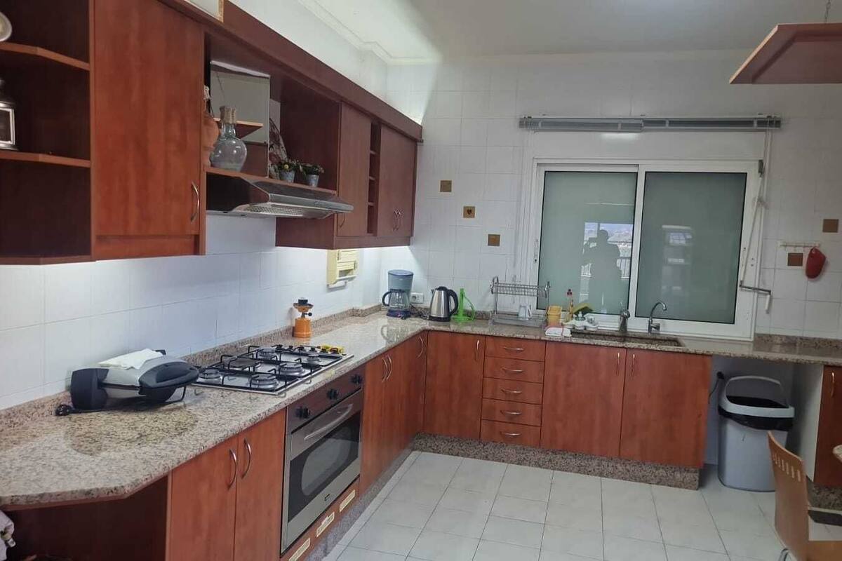 Une cuisine avec des meubles de rangement en bois, une cuisinière à gaz, un évier et une fenêtre.