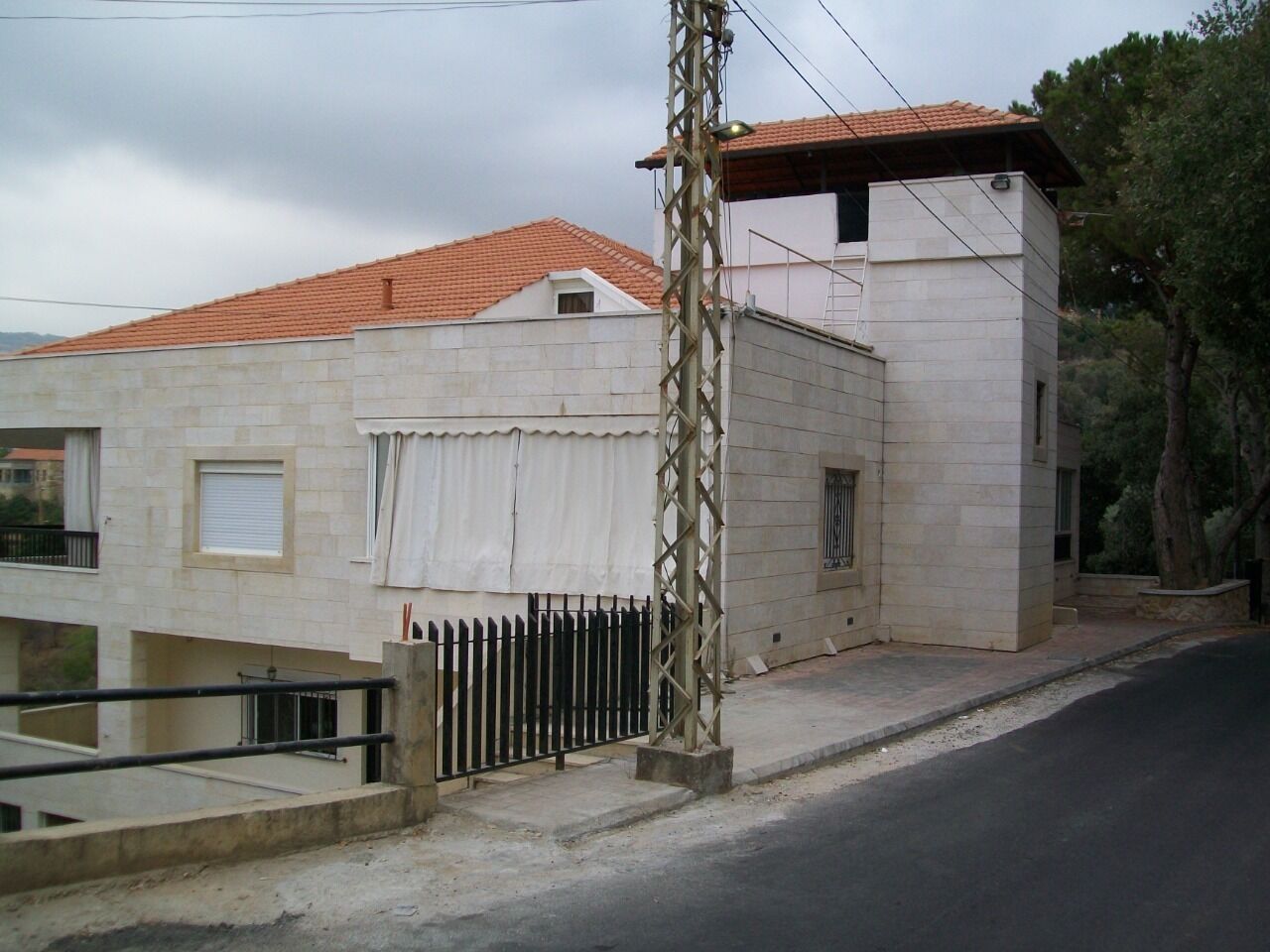 A two-story building with a red-tiled roof, a white exterior, and a black metal fence in front.