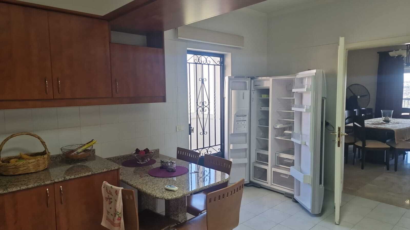 A kitchen with wooden cabinets, a granite countertop, a dining table with chairs, and a built-in refrigerator.