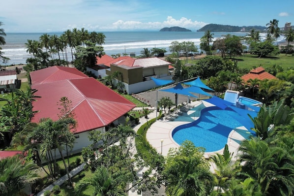 A resort with a swimming pool, red-roofed buildings, and a view of the ocean. - Luxury Beachfront Retreat – 13BR Private Resort with Pool in Jacó (Jaco)