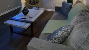 A living room with a sofa, a coffee table, and a lamp. There is a kitchen visible in the background. - The Music Row Getaway (Nashville)