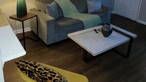 A living room with a sofa, a coffee table, a lamp, a chair, and a door. - The Music Row Getaway (Nashville)