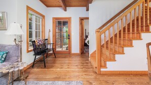 Un escalier en bois menant à un deuxième étage, un canapé agrémenté d’un plaid à motifs et un banc avec un coussin matelassé.