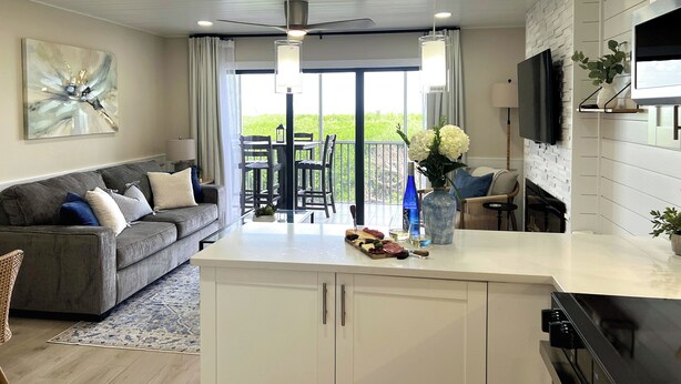 A modern kitchen with a dining area, a ceiling fan, and a view of greenery outside.