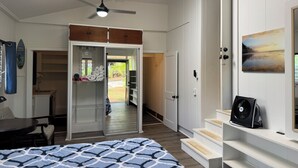 Un dormitorio con cama, ventilador de techo, vista al patio trasero y una escalera que sube a un nivel superior.