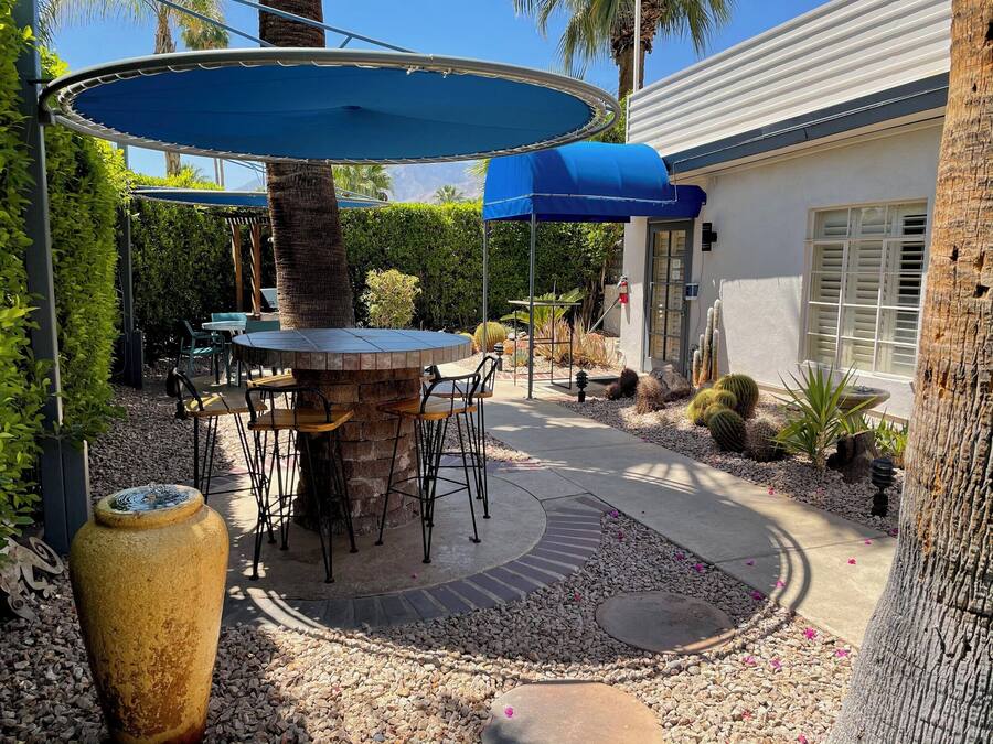 Un patio al aire libre con una mesa redonda y sillas, rodeado por una zona de grava con cactus y un jarrón grande.