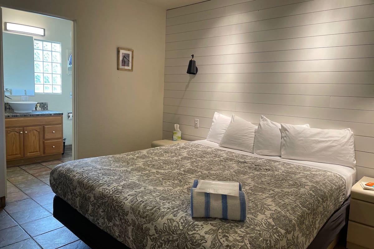 Ein Schlafzimmer mit einem großen Bett, einem Nachttisch, einer Wandlampe und einem Fenster mit Jalousien.