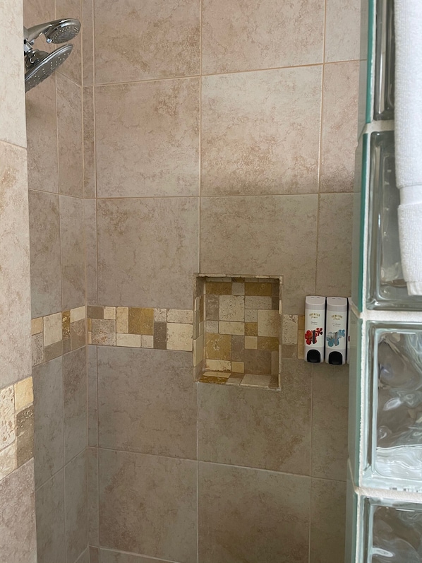 Un baño con azulejos color beige, una zona de ducha y dos dispensadores de jabón para manos.