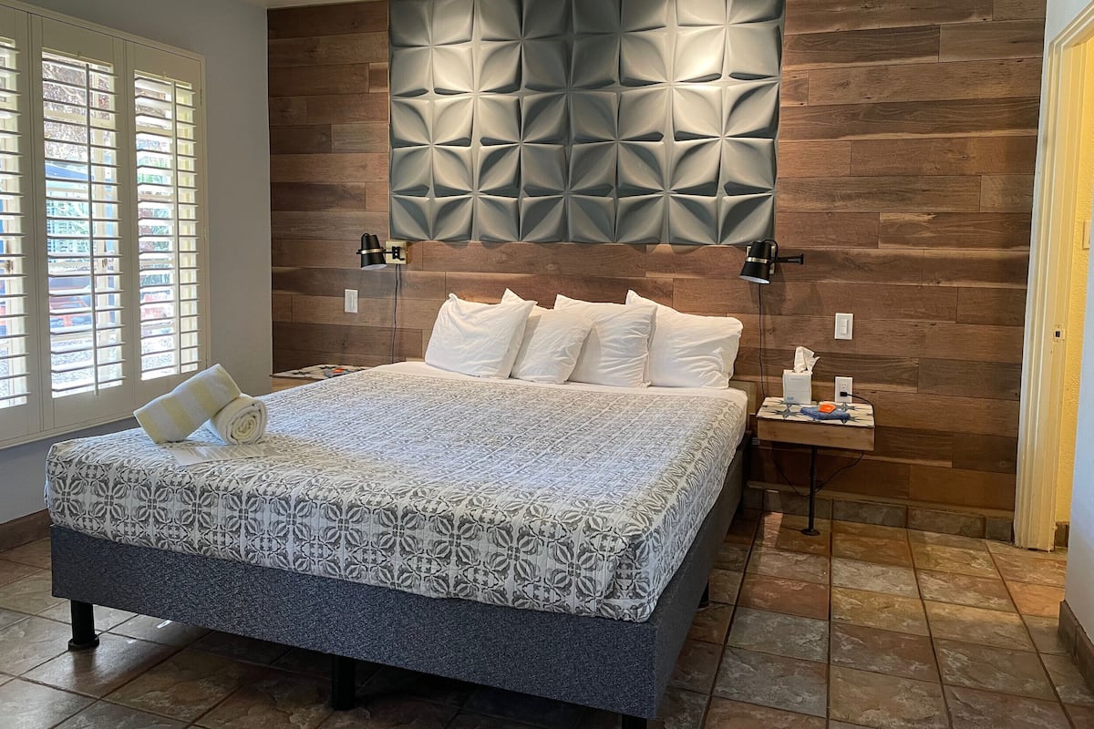 Ein modernes Schlafzimmer mit einem großen Bett, einer Wand im Holzoptik und einem Nachttisch mit Lampe.