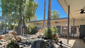 A landscaped outdoor area with a rock garden, palm trees, and a statue. - Desert Paradise Resort- Gay Men's Resort (Palm Springs)