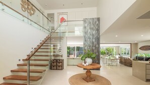 Un intérieur moderne avec un escalier en bois, une table ronde en bois ornée d’un vase, et un coin repas avec des chaises et une table.