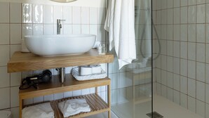 Une salle de bain moderne avec un grand lavabo ovale, un miroir rond, une douche en verre et un meuble-lavabo en bois agrémenté de serviettes.