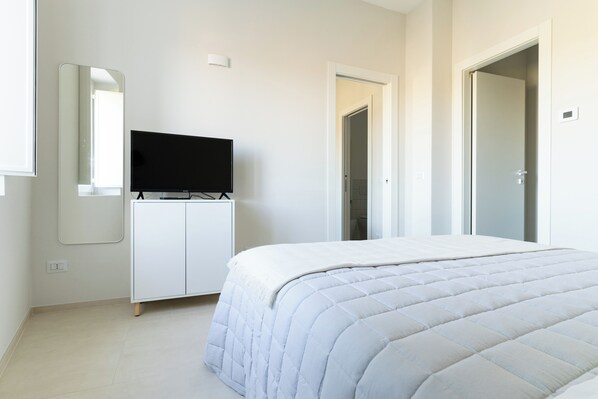 Une chambre à coucher avec un lit, un téléviseur posé sur un meuble, un miroir et une armoire.