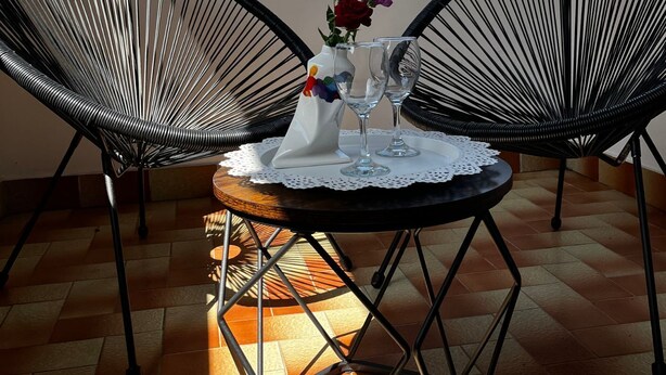 A patio with two black wire-framed chairs, a small round table with a lace doily, and a vase with flowers and wine glasses. - Family friendly Private pool Quiet location, own garden Walking distance to Lake Balaton (Balatonföldvár)