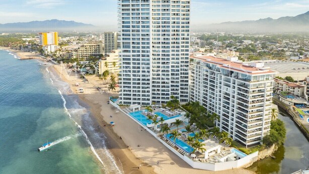 Un hotel de gran altura con múltiples balcones, ubicación frente a la playa y zona de piscina.