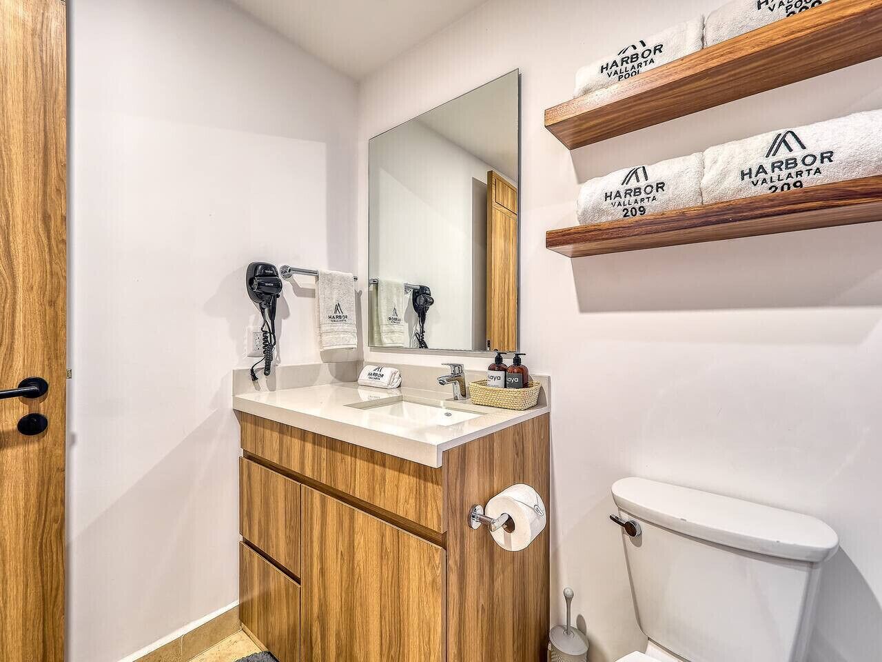 A bathroom with a wooden vanity, a mirror, a toilet, and shelves with towels.