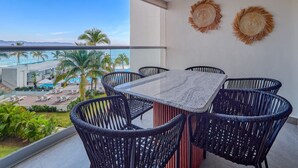 Un balcón con mesa y sillas, con vistas a una piscina y palmeras.