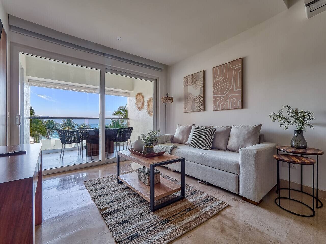 Un salon moderne avec un canapé, une table basse et une vue sur un espace de détente extérieur, accessible par une porte-fenêtre coulissante.