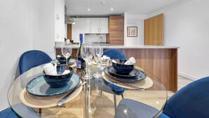 A modern dining area with a glass table, blue chairs, and a kitchen in the background. - Liverpool Street Retreat (London)