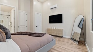 Un dormitorio moderno con cama, televisor, espejo y armario.