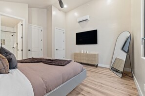 Un dormitorio moderno con cama, televisor, espejo y armario.