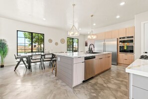 A modern kitchen with a large island, stainless steel appliances, and a dining area with a view. - Brand New Home! Its about time to have a beautiful pool area, spacious 7 bedroom home. (Hurricane)