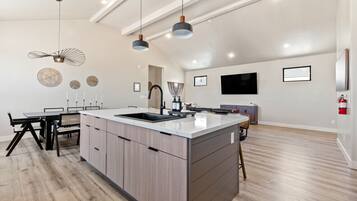 A modern kitchen with a central island, pendant lighting, and a dining area with a table and chairs.