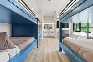 Une chambre avec des lits superposés, et une cuisine en arrière-plan.