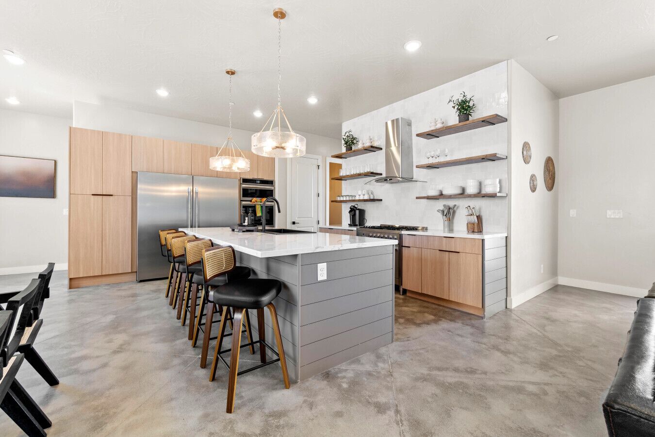 Een moderne keuken met een centraal eiland, krukken, roestvrijstalen apparatuur en open kasten.