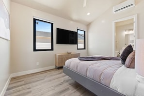 A modern bedroom with a bed, a flat-screen TV, a radiator, and a window with blinds. - Brand New Home! Its about time to have a beautiful pool area, spacious 7 bedroom home. (Hurricane)