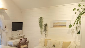 Un salon avec un canapé blanc, un plancher en bois, un ventilateur de plafond, une télévision et une plante.