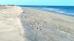 Une plage avec un chemin en béton et des empreintes de pas qui mènent à l’eau.
