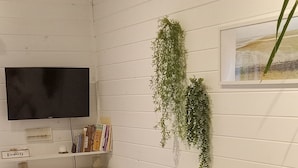 Un salon chaleureux avec un canapé blanc, une chaise en bois, un téléviseur et une grande plante.