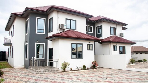 A two-story residential building with a balcony, air conditioning units, and a paved driveway.