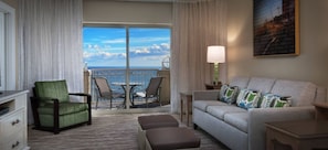Ein Hotelzimmer mit Balkon, einem grünen Sessel, einem grauen Sofa und einem Bild an der Wand.