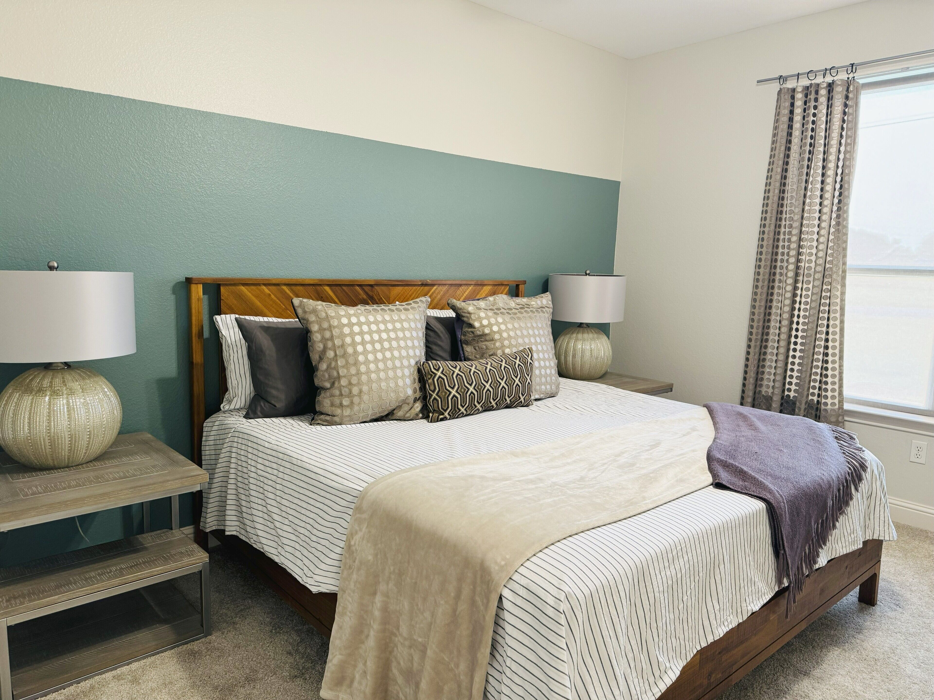 A bedroom with a bed, two bedside tables, a lamp, and a window with curtains.