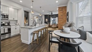 A modern kitchen with white cabinets, a central island with stools, and a dining area with a round table and chairs. - Hot Tub-Sauna-Bar-Gym-4BR-Sleeps 8 (Columbus)